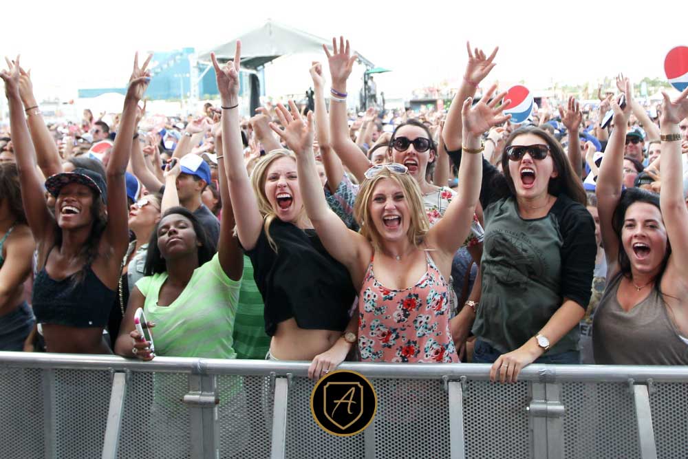 A group of enthusiastic women cheer and raise their hands behind a metal barrier at an outdoor concert, highlighting the need for security like How-Executive-Protection-Reduces-Risk-3 to ensure crowd safety.