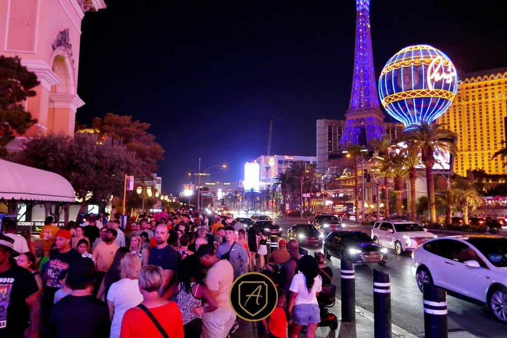 A large crowd walks along the busy Las Vegas Strip at night, with neon lights, cars, and the illuminated Eiffel Tower replica in the background—an example of environments discussed in How-Executive-Protection-Reduces-Risk-4.