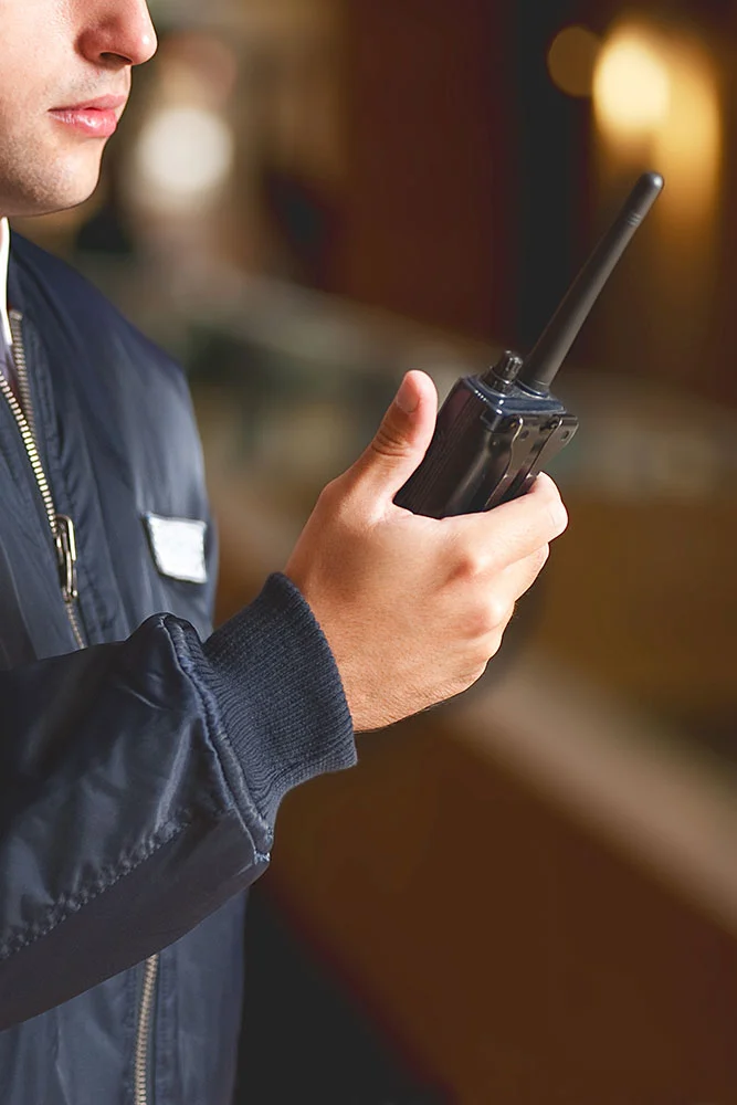 A person in a dark jacket holds a walkie-talkie, seemingly communicating; the blurred background highlights Executive Protection & Bodyguards in Las Vegas from Alexios Security Solutions—medium-carousel-2.