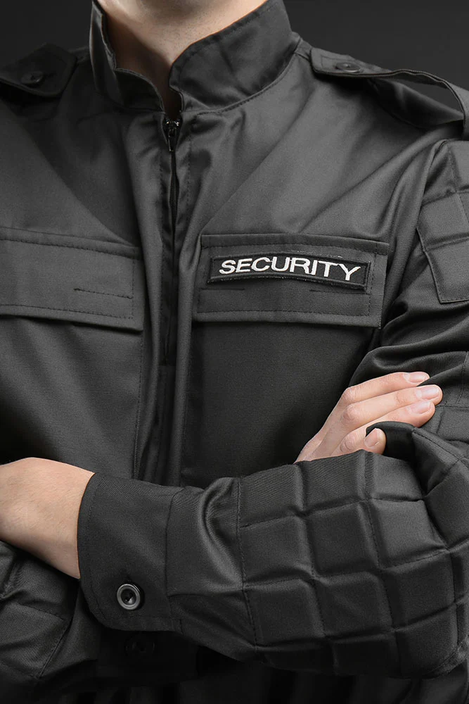 A person in a black security uniform stands with arms crossed, SECURITY patch visible. The dark background adds intensity—capturing medium-carousel-3 by Alexios Security Solutions in Las Vegas.