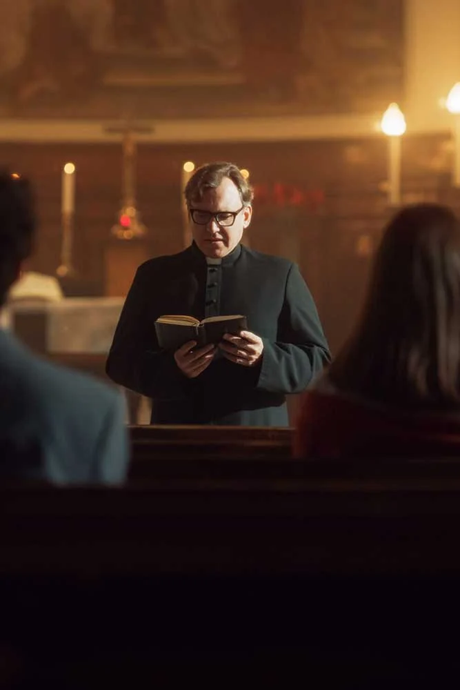 A priest in black robes addresses two pew-seated individuals in a softly lit church, surrounded by candles and religious symbols—a tranquil scene contrasting the security focus of medium-carousel-6.