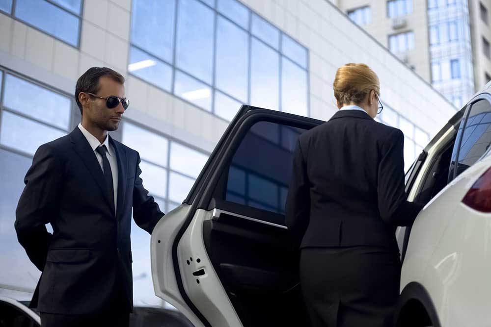 In security-image-3, an Alexios Security Solutions bodyguard in a suit and sunglasses provides executive protection in Las Vegas, holding the car door open for a businesswoman outside a modern office building. In security-image-3, an Alexios Security Solutions bodyguard in a suit and sunglasses provides executive protection in Las Vegas, holding the car door open for a businesswoman outside a modern office building.