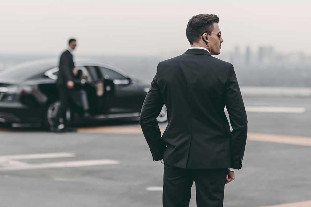 Two men in suits stand by a black car—one wearing an earpiece, the other by the open door—showcasing professionalism typical of Executive Protection & Bodyguards in Las Vegas. Product: security-image-5 | Alexios Security Solutions.