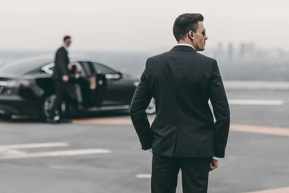 Two men in suits stand by a black car—one wearing an earpiece, the other by the open door—showcasing professionalism typical of Executive Protection & Bodyguards in Las Vegas. Product: security-image-5 | Alexios Security Solutions.