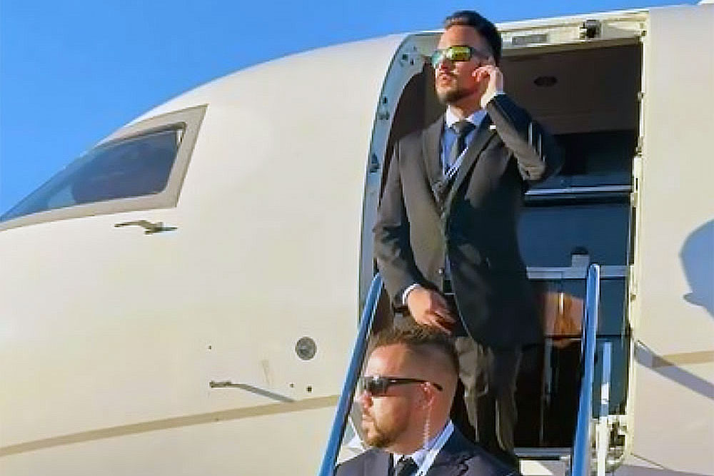 Two alert, professional men in suits and sunglasses stand on private jet steps—one adjusting an earpiece—representing security-off-airplane-2 executive protection & bodyguard services from Alexios Security Solutions in Las Vegas.