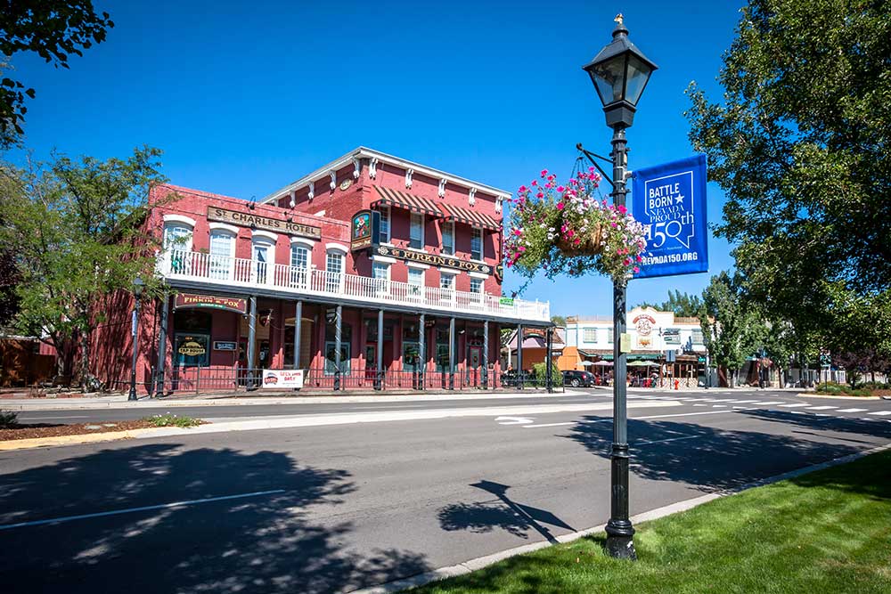 A historic red brick building with white trim and balconies stands on a quiet, tree-lined Reno street. A Battle Born Month banner hangs nearby, as Alexios-security-solutions-carson-city-nevada keeps the area secure.