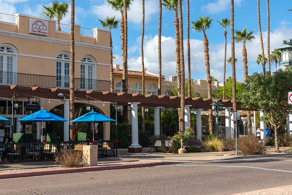 A sunny street scene in Reno features outdoor dining with blue umbrellas, palm trees, and a tan building. Alexios-security-solutions-chandler-arizona discreetly provides security for this vibrant setting under a clear blue sky. A sunny street scene in Reno features outdoor dining with blue umbrellas, palm trees, and a tan building. Alexios-security-solutions-chandler-arizona discreetly provides security for this vibrant setting under a clear blue sky.
