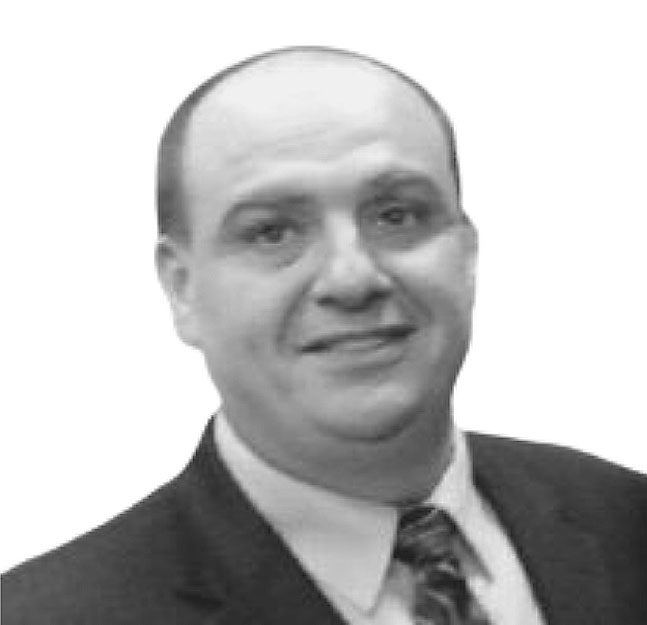 A man in a suit and tie smiles at the camera in this black and white photo with a plain white background, subtly showcasing the professionalism of antonios executive protection and personal security services.