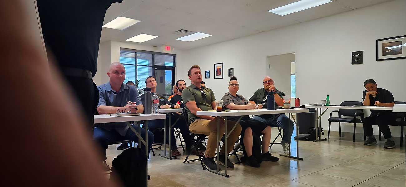 Adults sit at tables in a well-lit classroom with tile floors and framed pictures, engaging in a Nevada concealed carry permit training session. Some take notes or hold drinks. Image: ccw-certification-main-image. | Executive Protection & Bodyguards in Las Vegas | Alexios Adults sit at tables in a well-lit classroom with tile floors and framed pictures, engaging in a Nevada concealed carry permit training session. Some take notes or hold drinks. Image: ccw-certification-main-image. | Executive Protection & Bodyguards in Las Vegas | Alexios