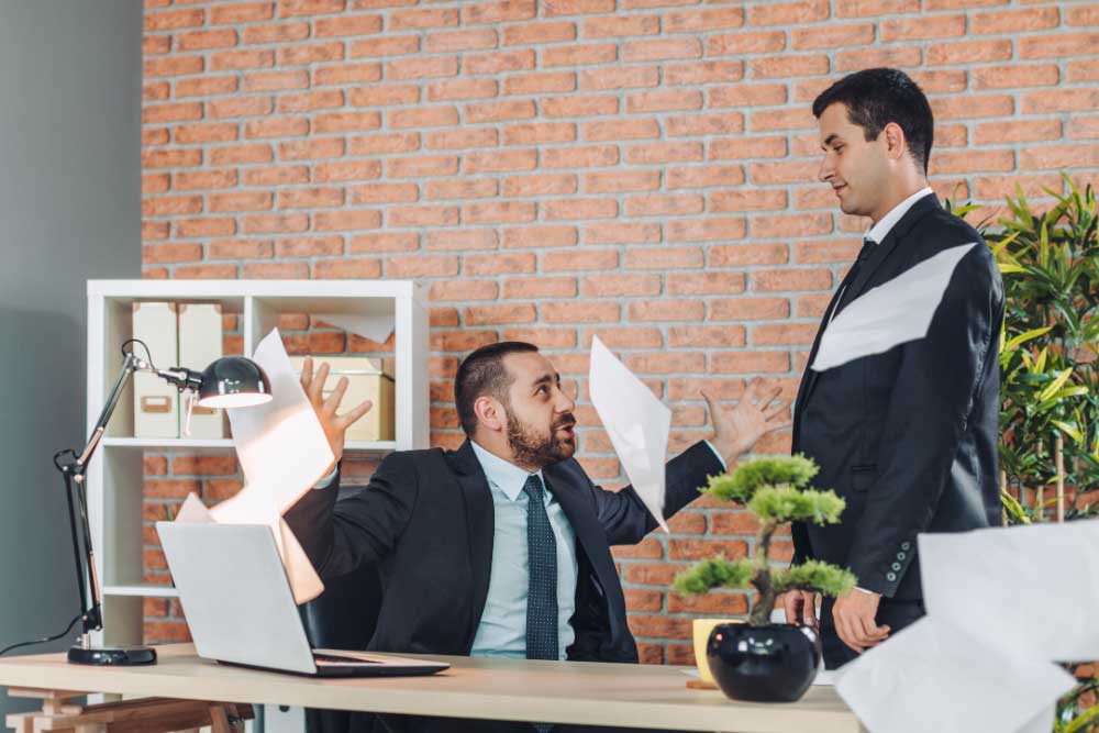 Two men in suits argue in an office, with one angrily throwing papers. This shows the importance of using hostile-termination-training-6 for workplace violence training and secure employee separation to keep offices safe. Two men in suits argue in an office, with one angrily throwing papers. This shows the importance of using hostile-termination-training-6 for workplace violence training and secure employee separation to keep offices safe.