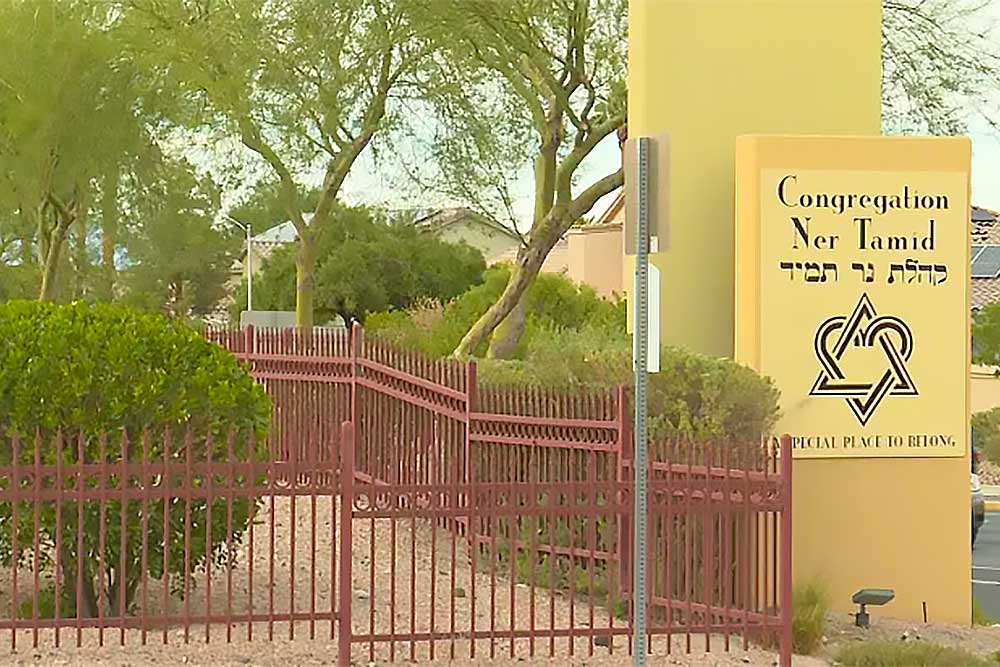 A yellow house-of-worship-security-5 sign with Hebrew text and a Star of David stands by the entrance of Congregation Ner Tamid near a red fence, reflecting increased security for houses of worship. A yellow house-of-worship-security-5 sign with Hebrew text and a Star of David stands by the entrance of Congregation Ner Tamid near a red fence, reflecting increased security for houses of worship.