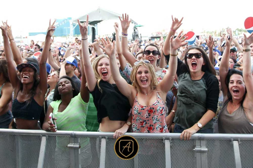 A group of enthusiastic women cheer and raise their hands behind a metal barrier at an outdoor concert, highlighting the need for security like How-Executive-Protection-Reduces-Risk-3 to ensure crowd safety.