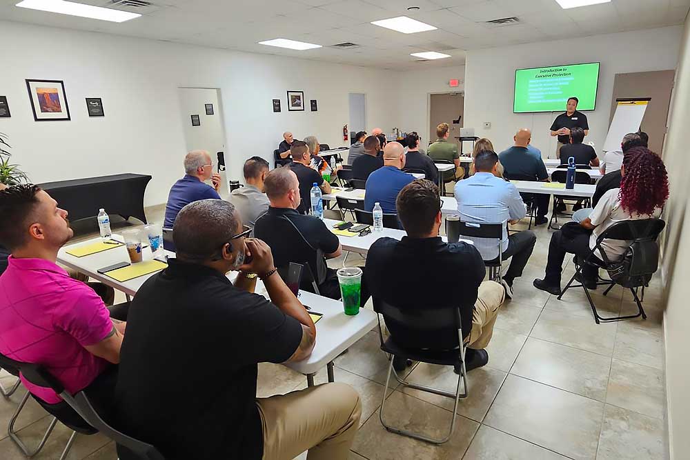 Adults attend a behavioral intelligence session (training-carousel-8), seated at desks with notebooks and drinks, listening to an instructor in front of a screen. Framed art decorates the classroom walls.