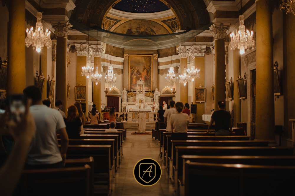 Attendees sit in wooden pews inside an ornate church with chandeliers, columns, and a painted ceiling during a ceremony, reflecting insights from "The-Importance-of-Worship-Security-in-Nevada-Communities-3. | Executive Protection & Bodyguards in Las Vegas | Alexios
