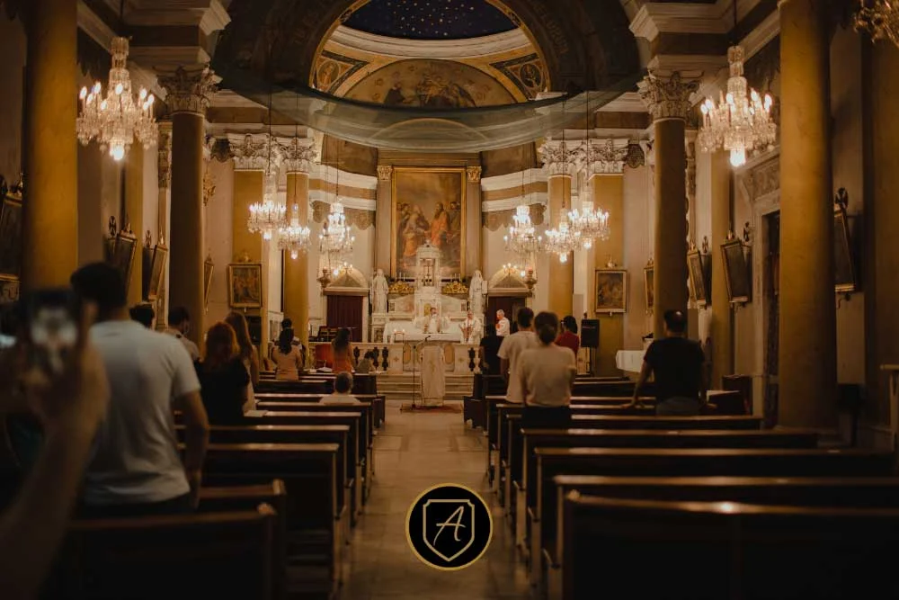 Attendees sit in wooden pews inside an ornate church with chandeliers, columns, and a painted ceiling during a ceremony, reflecting insights from "The-Importance-of-Worship-Security-in-Nevada-Communities-3. | Executive Protection & Bodyguards in Las Vegas | Alexios