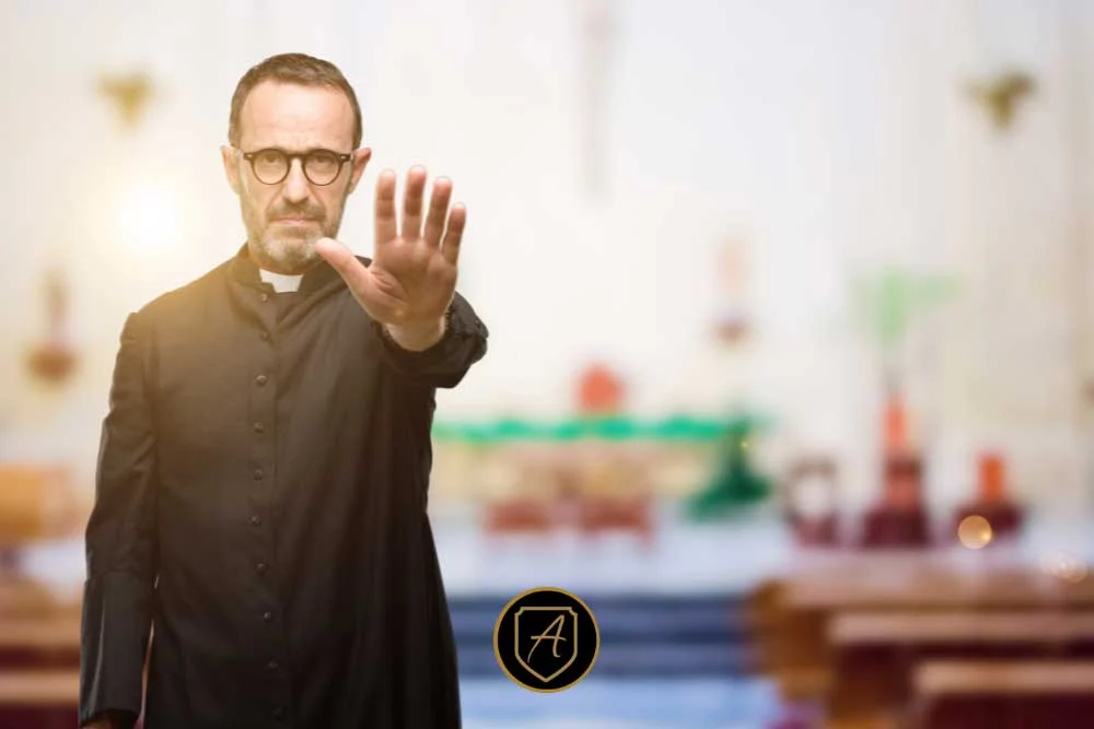 In "The-Importance-of-Worship-Security-in-Nevada-Communities-5," a priest in black robes stands in a church with his right hand raised, signaling stop. The blurred background reveals pews and an altar. | Executive Protection & Bodyguards in Las Vegas | Alexios